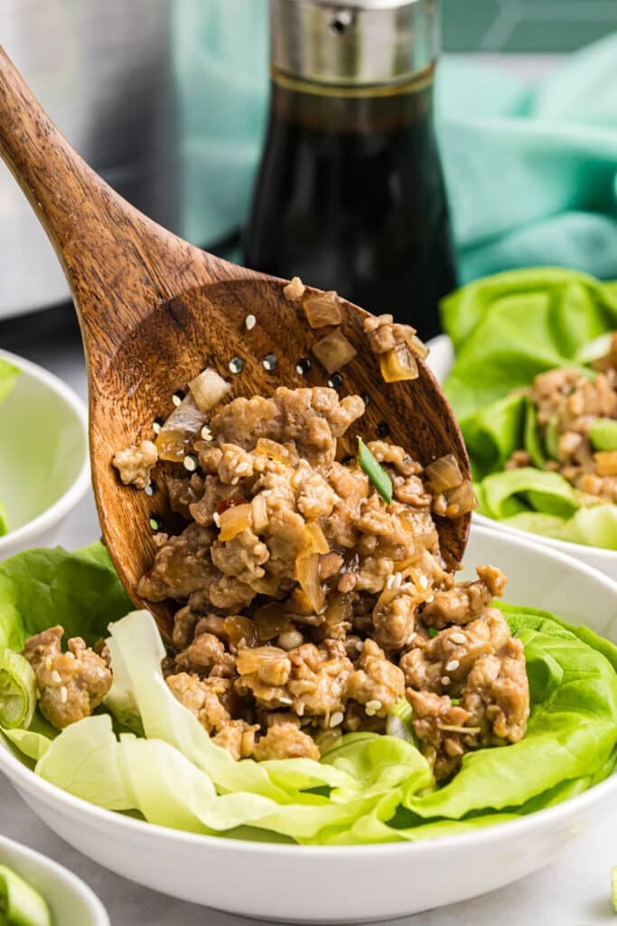 Wooden spoon scooping chicken mixture over lettuce wraps.