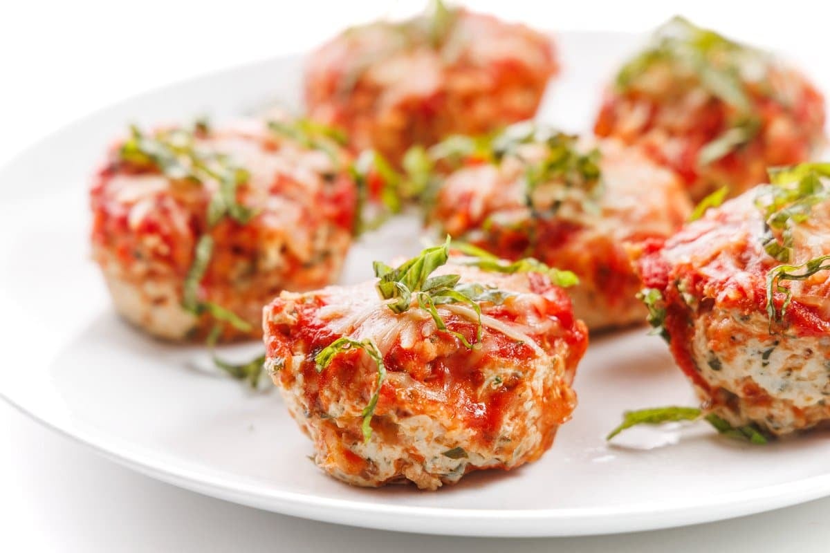 Chicken parm meatloaf muffins on a plate with fresh herbs.