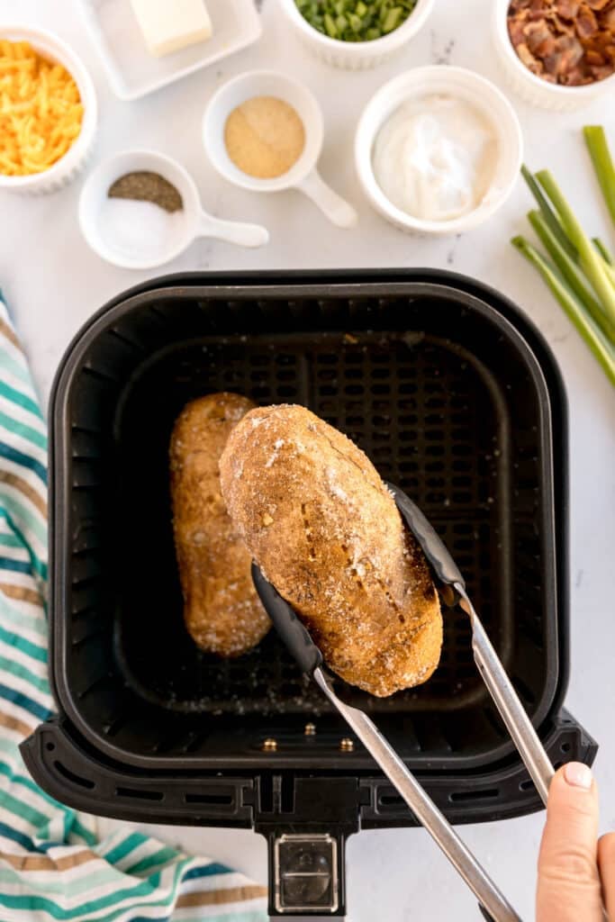 tongs lifting a potato from an air fryer.