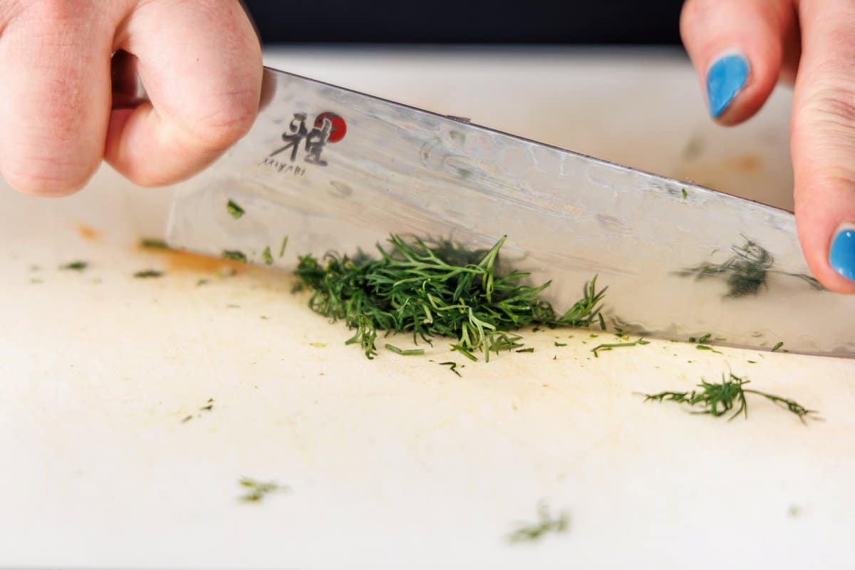 Liz mincing dill with a sharp knife.