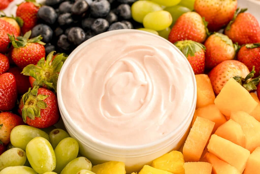 bowl of pink fruit dip surrounded by fresh fruit.