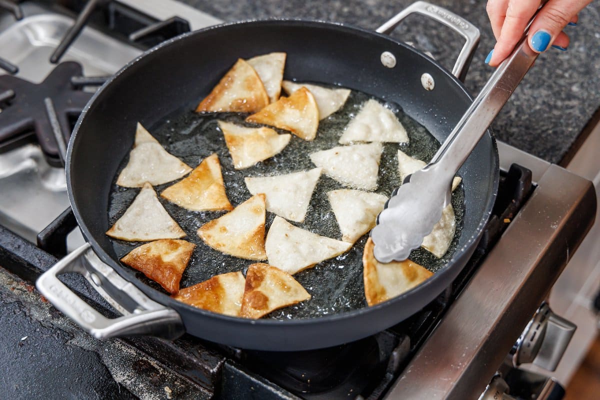 Frying tortilla triangles into chips in a pan on the stove.
