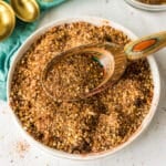 A bowl of homemade Montreal steak seasoning with a rustic wooden spoon scooping some up.