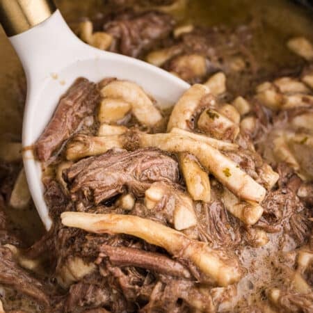 spoon scooping beef and noodles from a crockpot.
