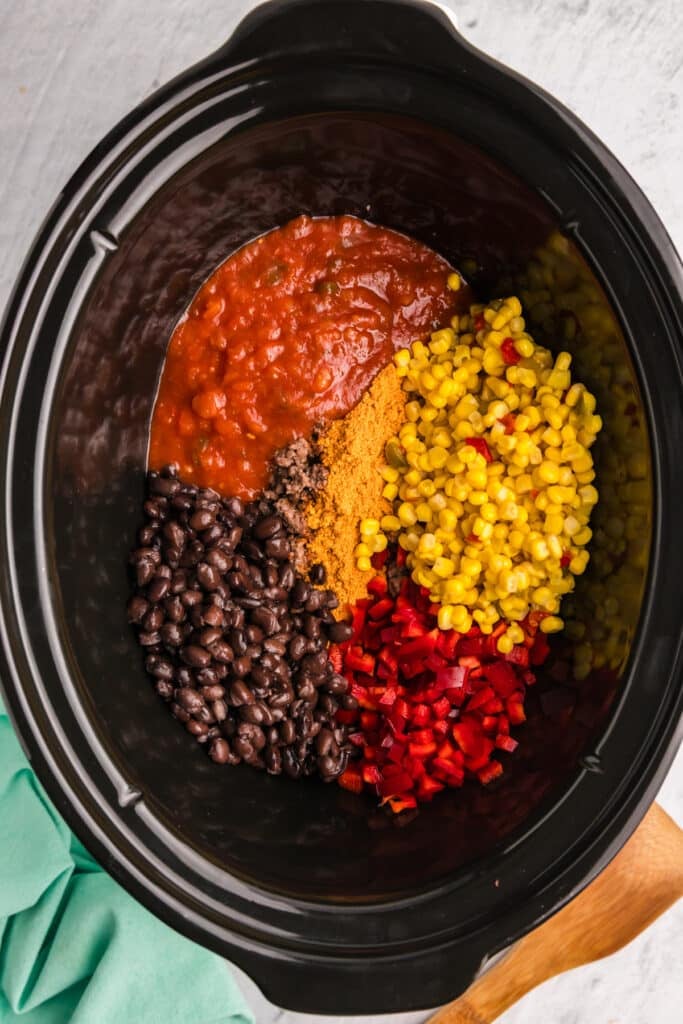 overhead shot of black beans, corn, diced peppers & tomatoes in a slow cooker.