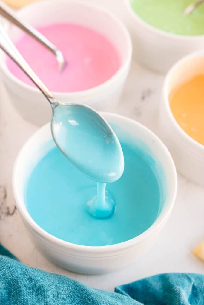 Spoon lifting blue icing from a bowl.