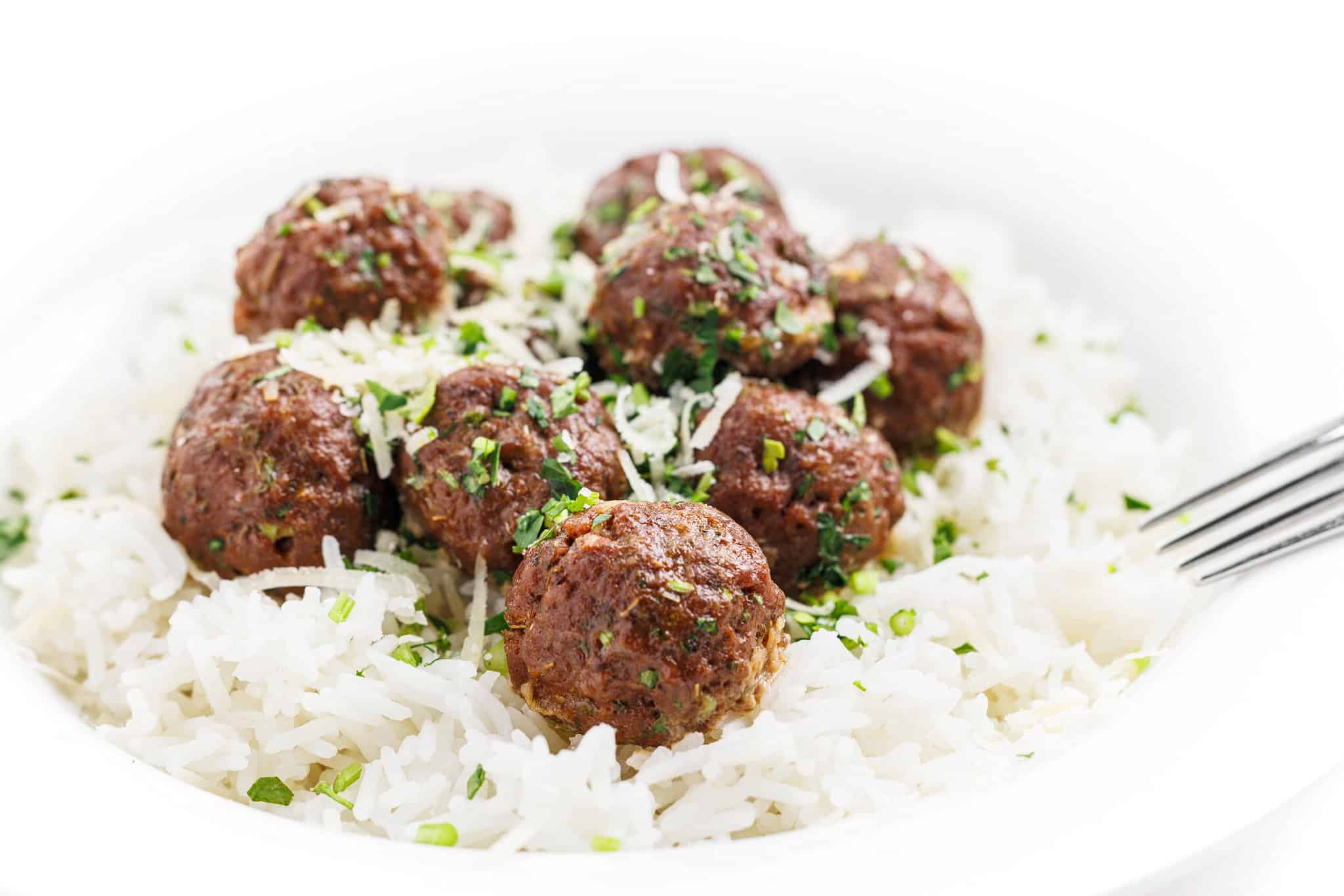 Plate with white rice topped with keftedes baked greek meatballs, with a fork.