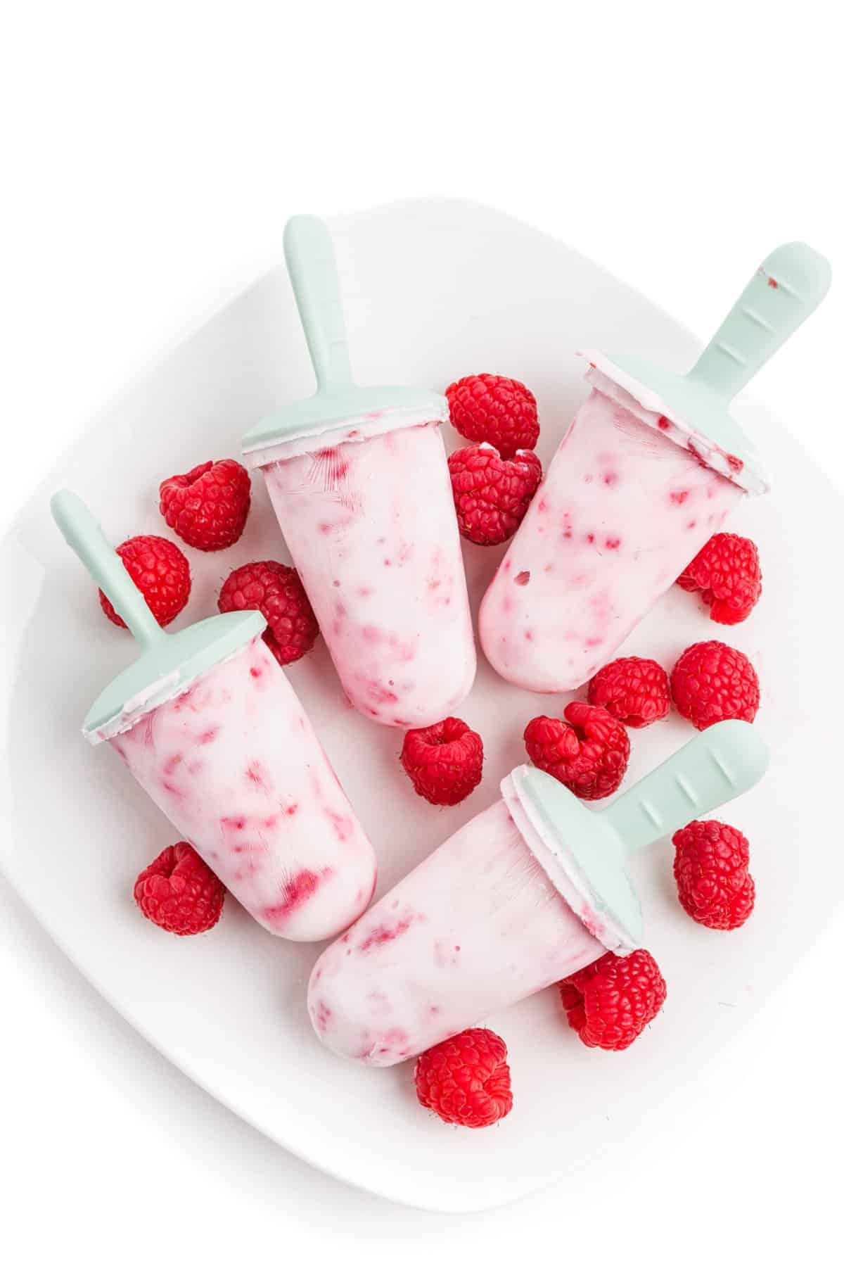 Raspberry Greek yogurt popsicles on a plate with fresh raspberries.