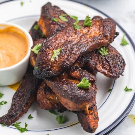 A plate of blackened chicken tenders with a side of dipping sauce.