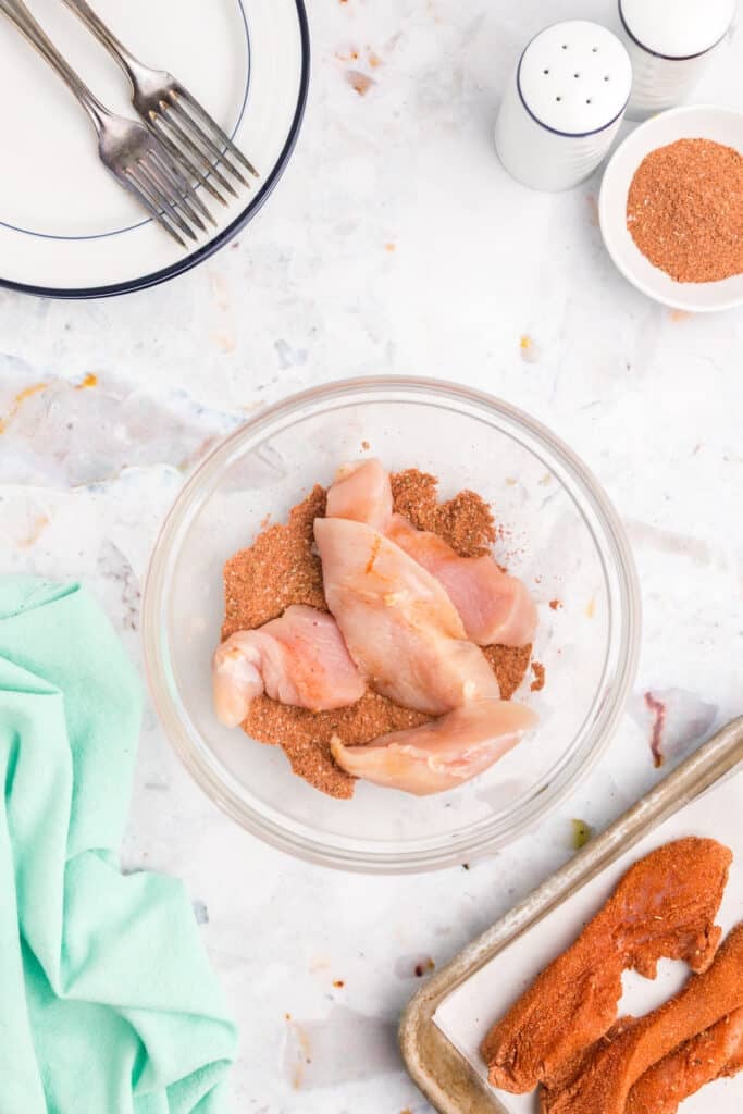 A bowl of raw chicken tenders coated in blackened seasoning.