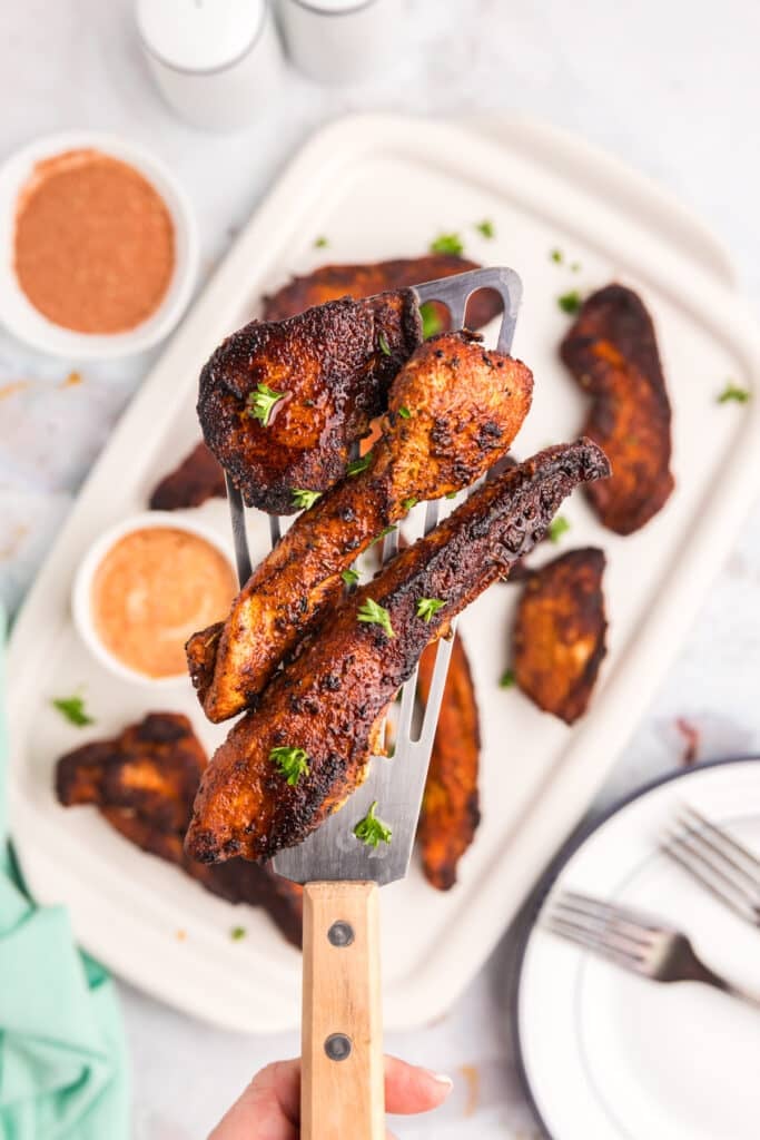 A spatula lifting blackened chicken tenders from a plate.