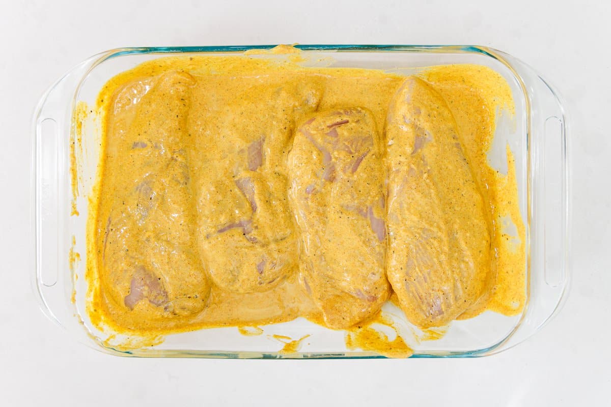 Chicken in a glass baking dish covered in Indian spiced marinade.