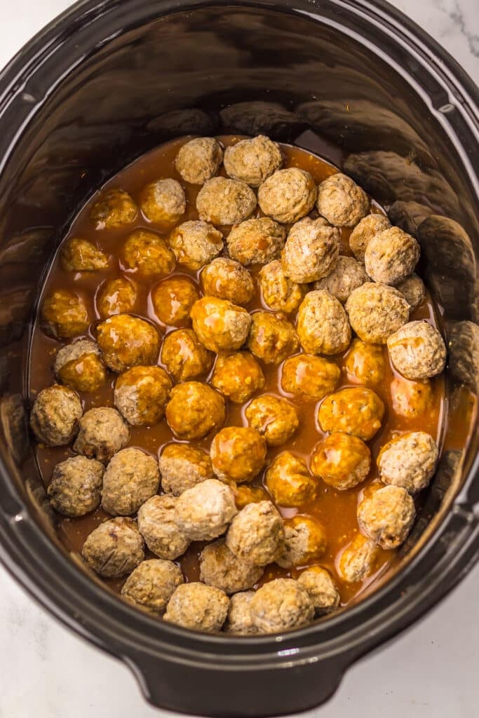 sauce poured over frozen meatballs in a black slow cooker.