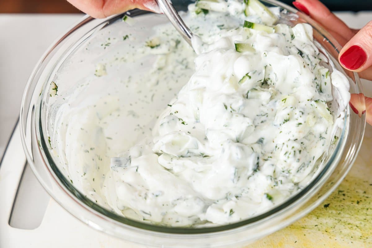 Stirring tzatziki sauce in a large glass bowl.