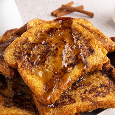 Close-up of stacked French toast with syrup on top and cinnamon sticks in the background.