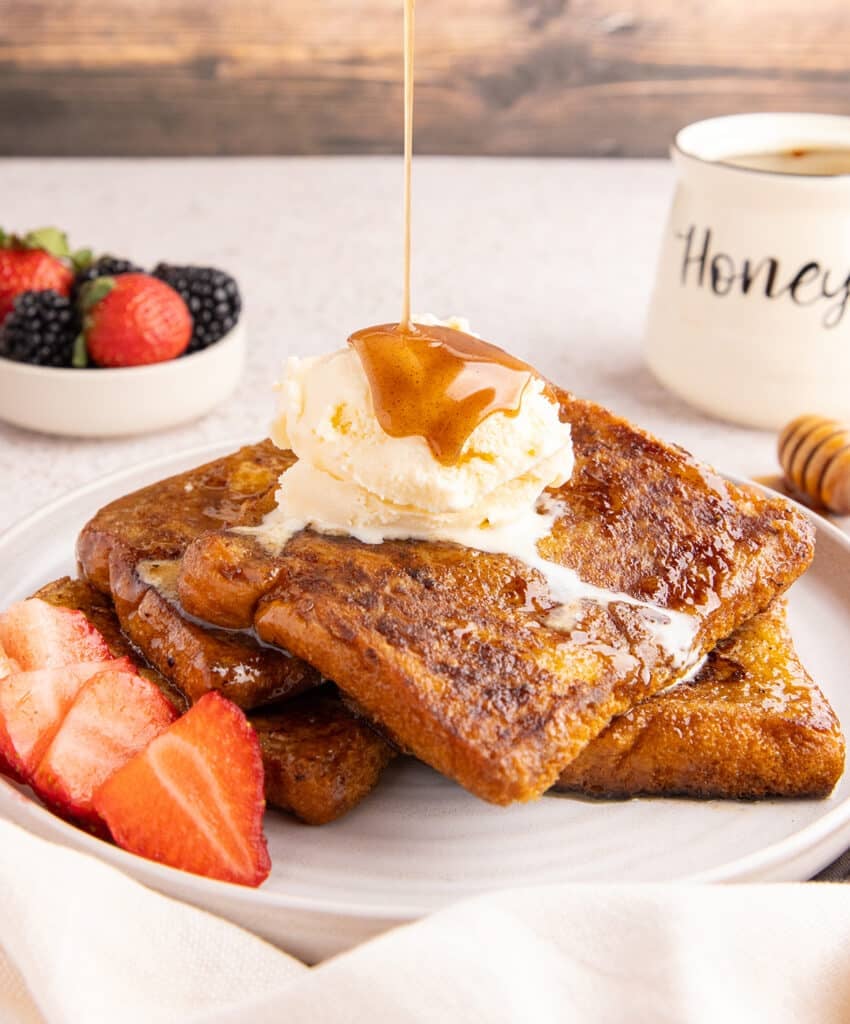 French toast topped with a scoop of vanilla ice cream and honey syrup being drizzled over, served with fresh berries.