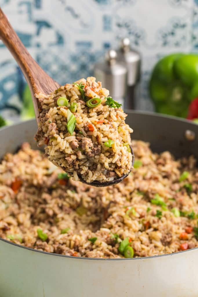 Spoon lifting a serving of cooked dirty rice from the pot.