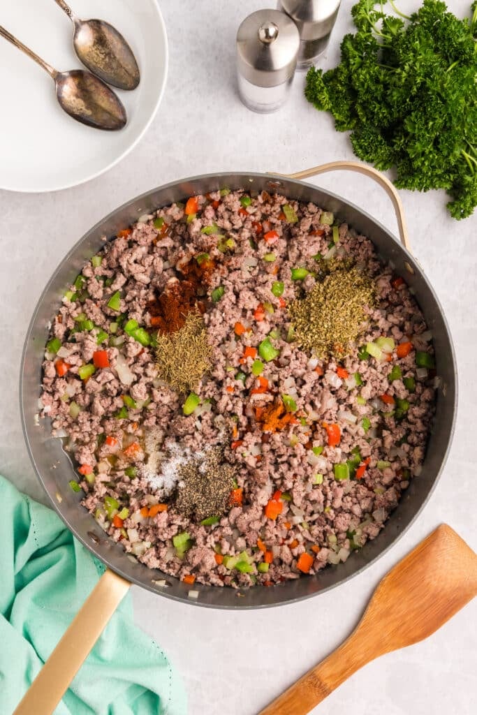 Ground meat and veggies topped with spices in a skillet.