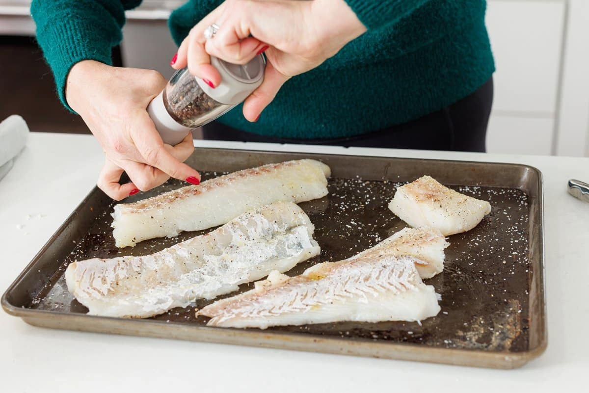 Seasoning white fish with a pepper grinder.