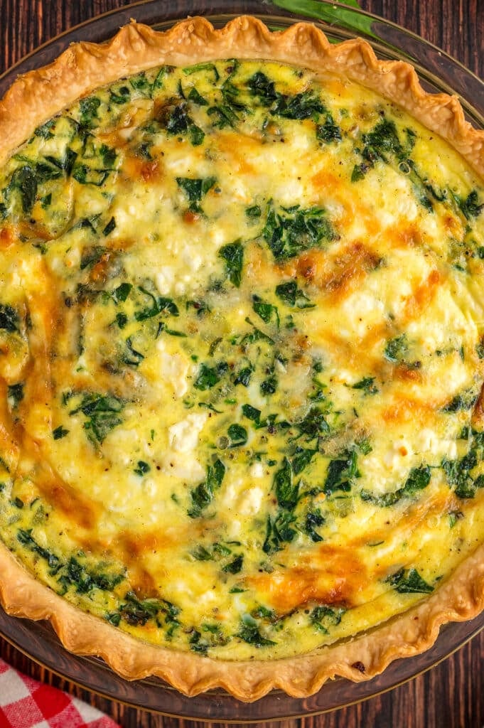 Close-up view of a golden baked spinach and cheese quiche inside a pie dish.