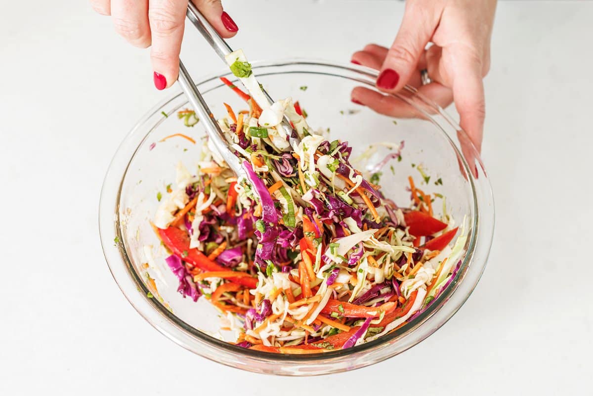 Tossing slaw in vinaigrette with tongs.