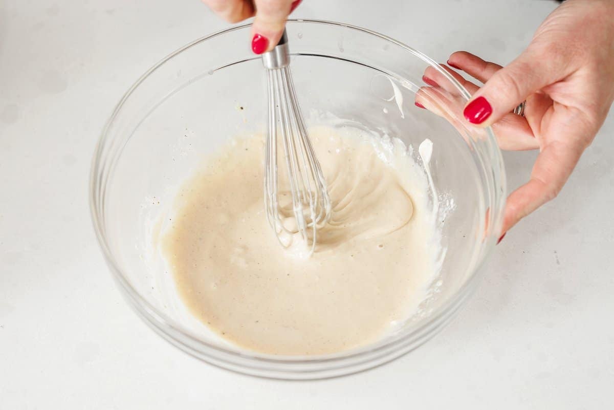 Whisking together tahini lemon sauce in a glass bowl.