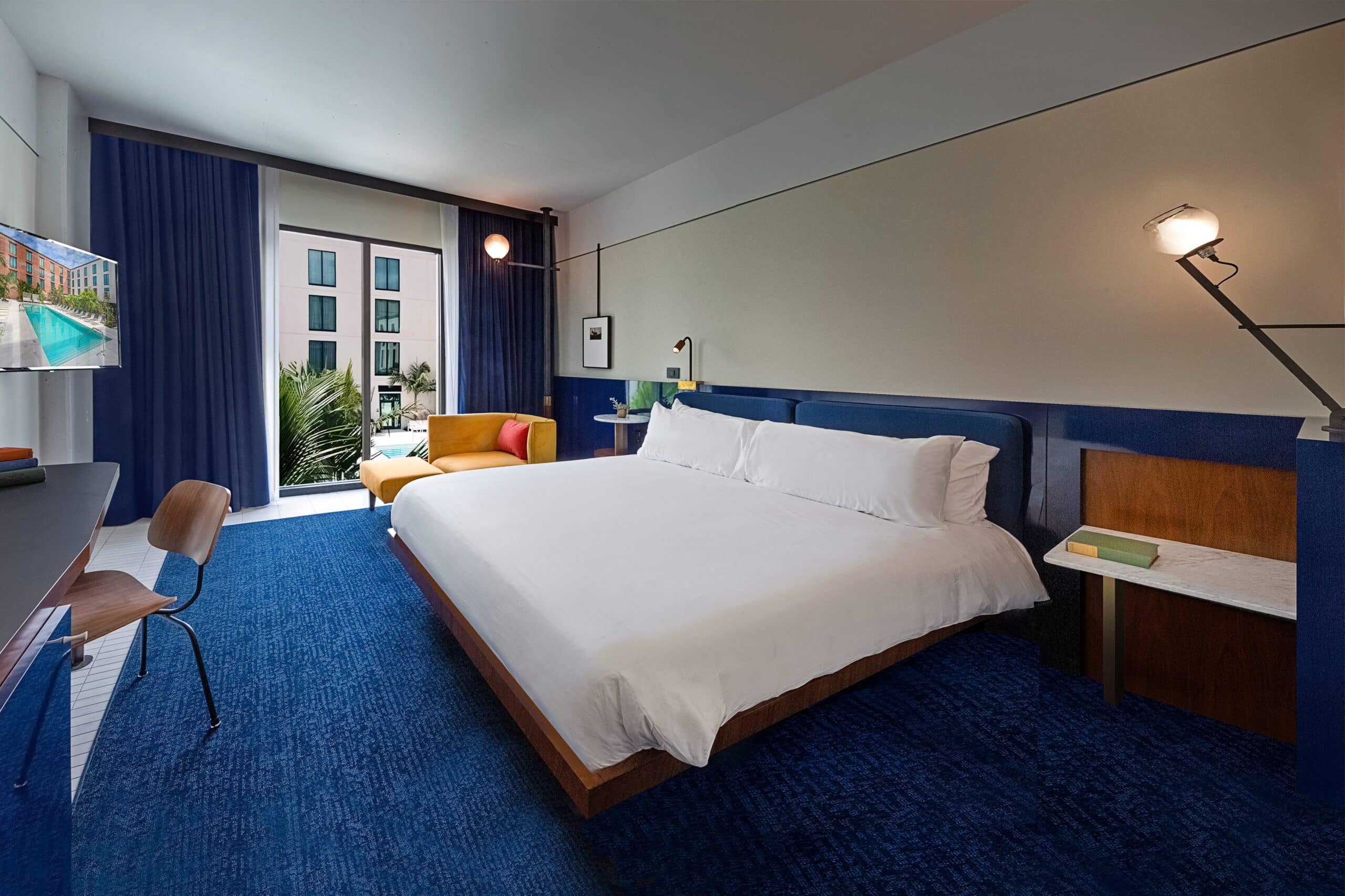 A made king sized bed in an elegant, clean hotel room with blue carpet and drapes.