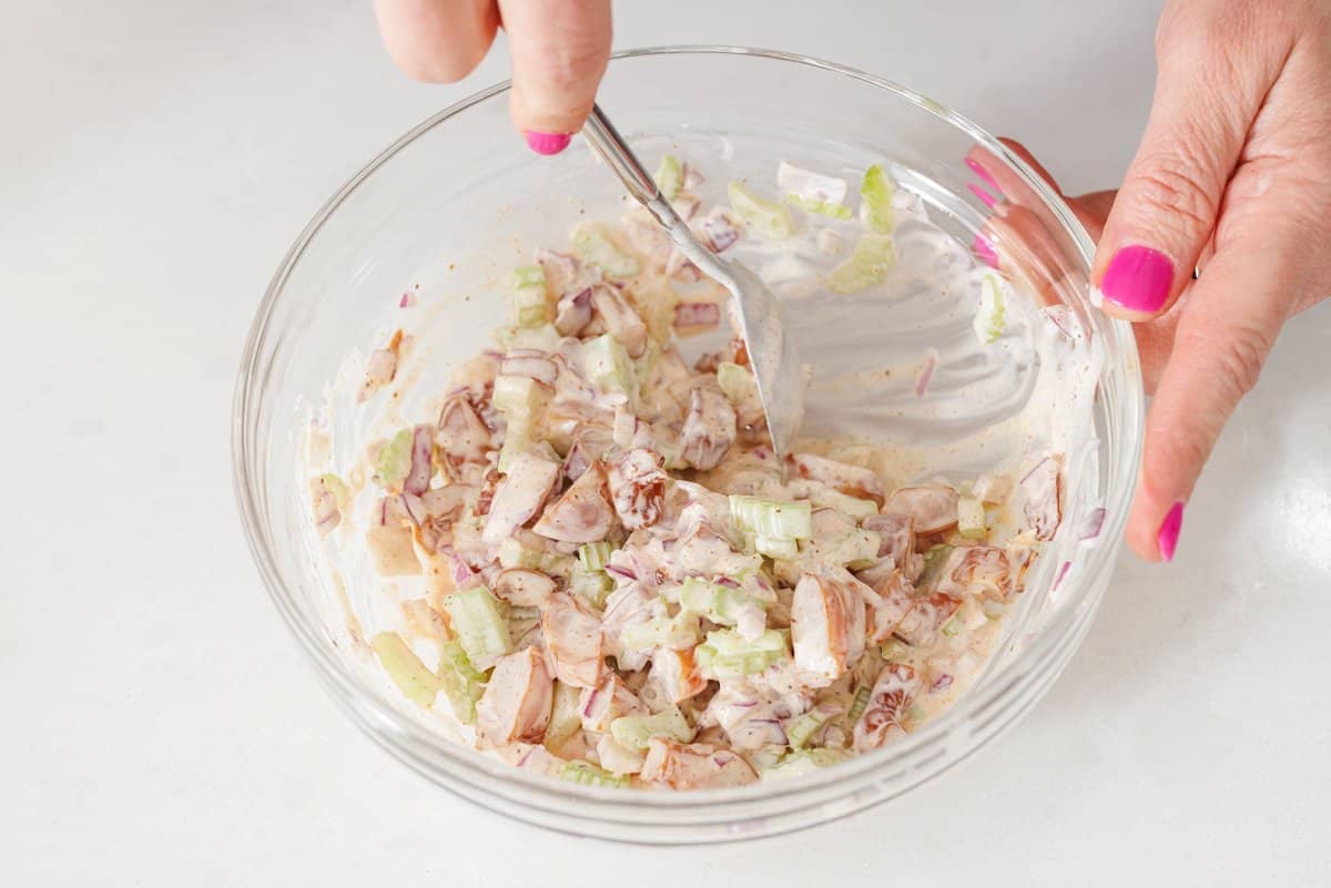 Tossing shrimp salad together with dressing with a spoon.