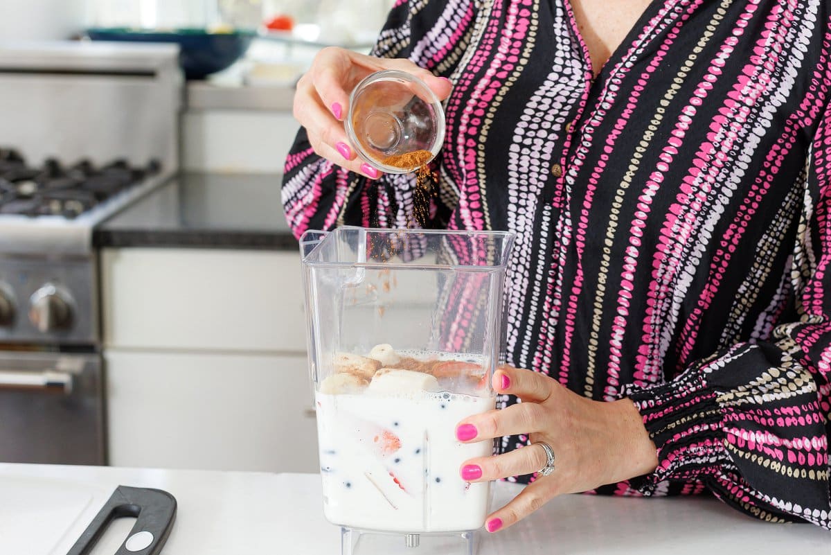 Adding cinnamon to a blender with yogurt and berries.