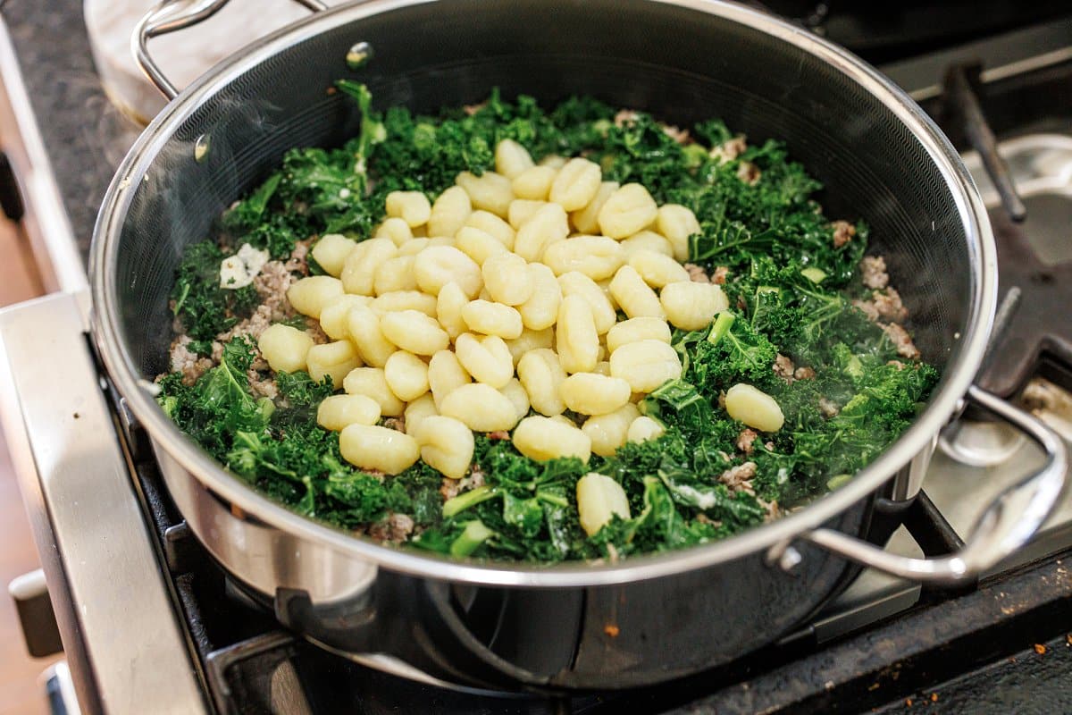 Adding cooked gnocchi to skillet of kale.