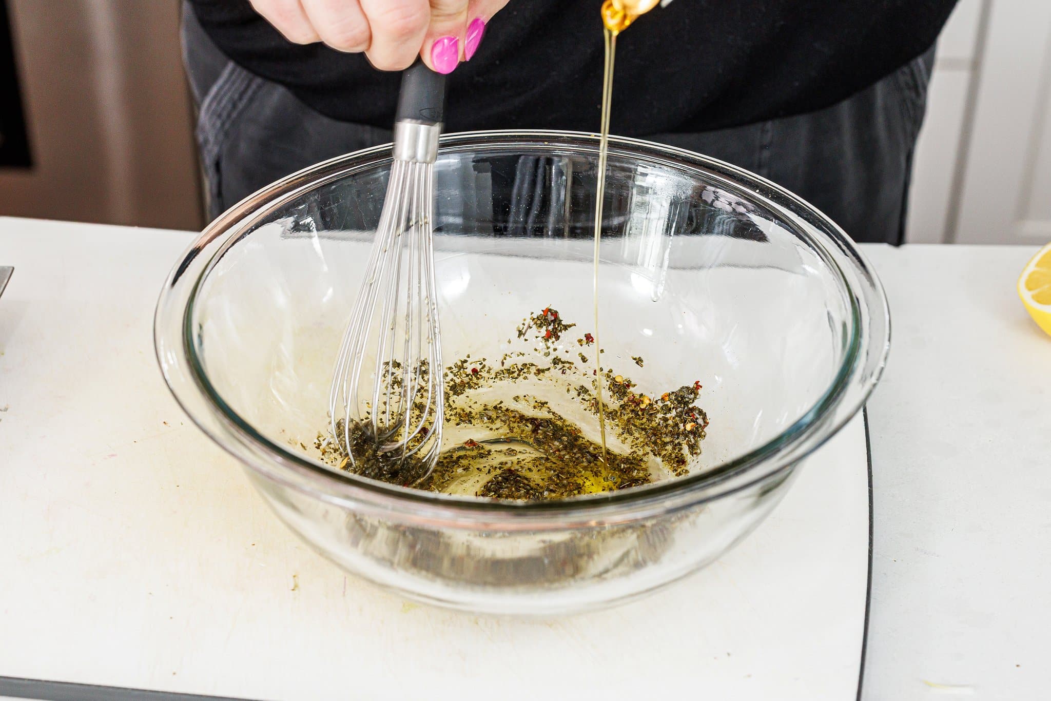 Adding olive oil to oregano and garlic  in a bowl.