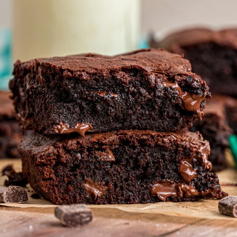 Stack of two thick, fudgy brownies with melty chocolate chunks on a wooden surface.