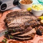 Sliced brisket on a cutting board with baked beans and potato salad.