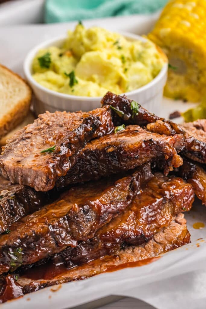 Close-up of several thick, glossy slices of beef brisket stacked on a tray.