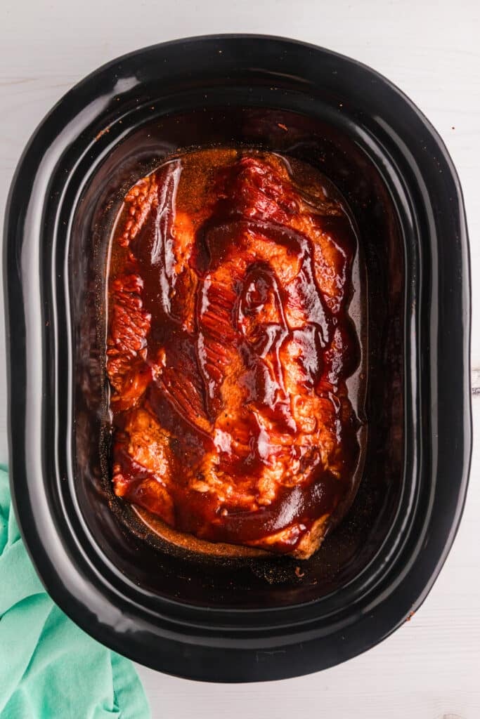 Uncooked brisket coated in BBQ sauce inside a slow cooker.