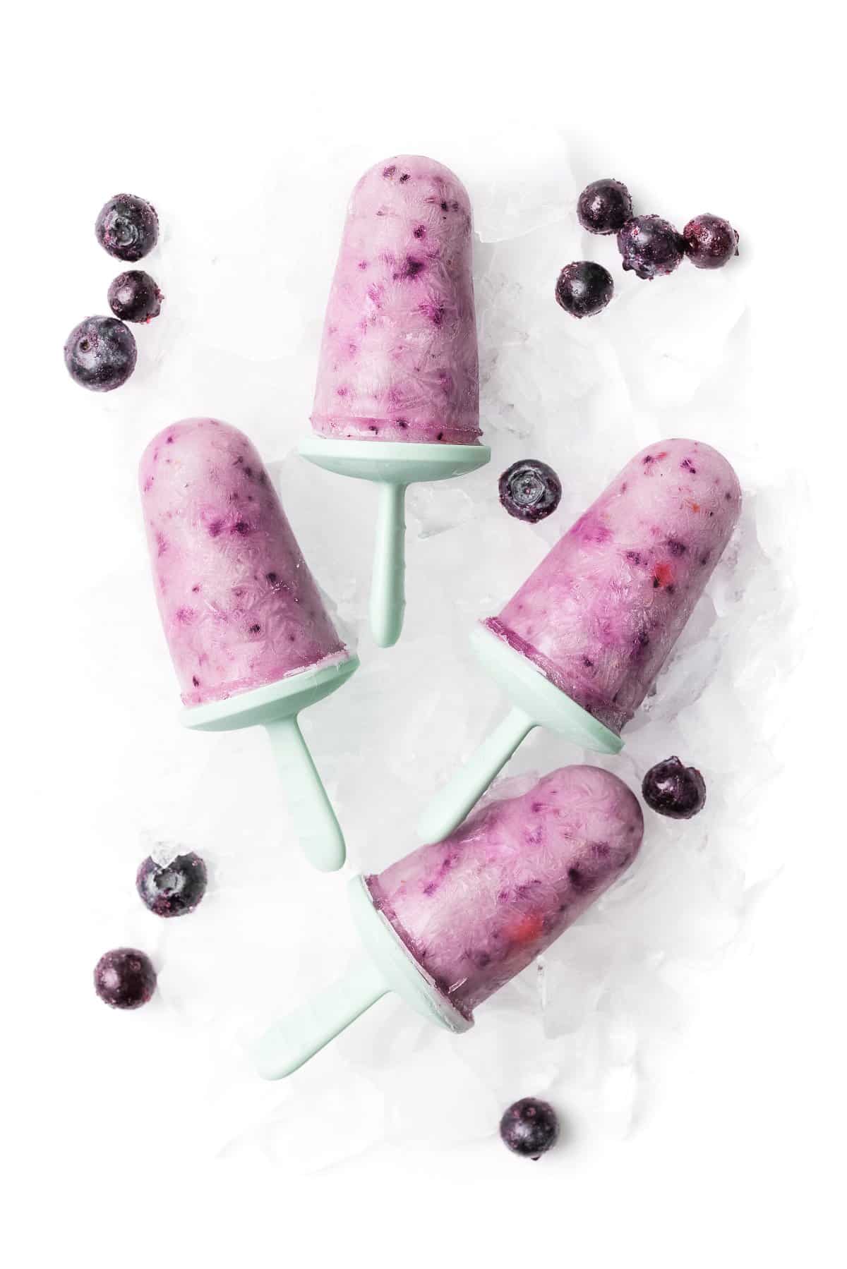 Greek yogurt berry popsicles removed from molds on a plate of ice.