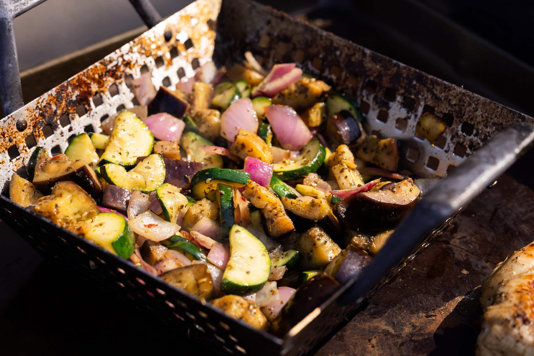Veggies cooking on grill in a grill basket.