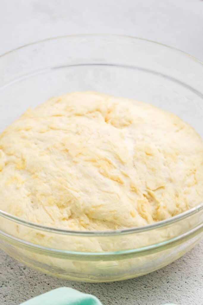 Risen dough in a clear glass bowl on a light countertop.