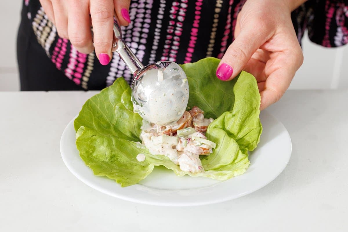Using an ice cream scoop to scoop shrimp salad onto a leaf of lettuce.