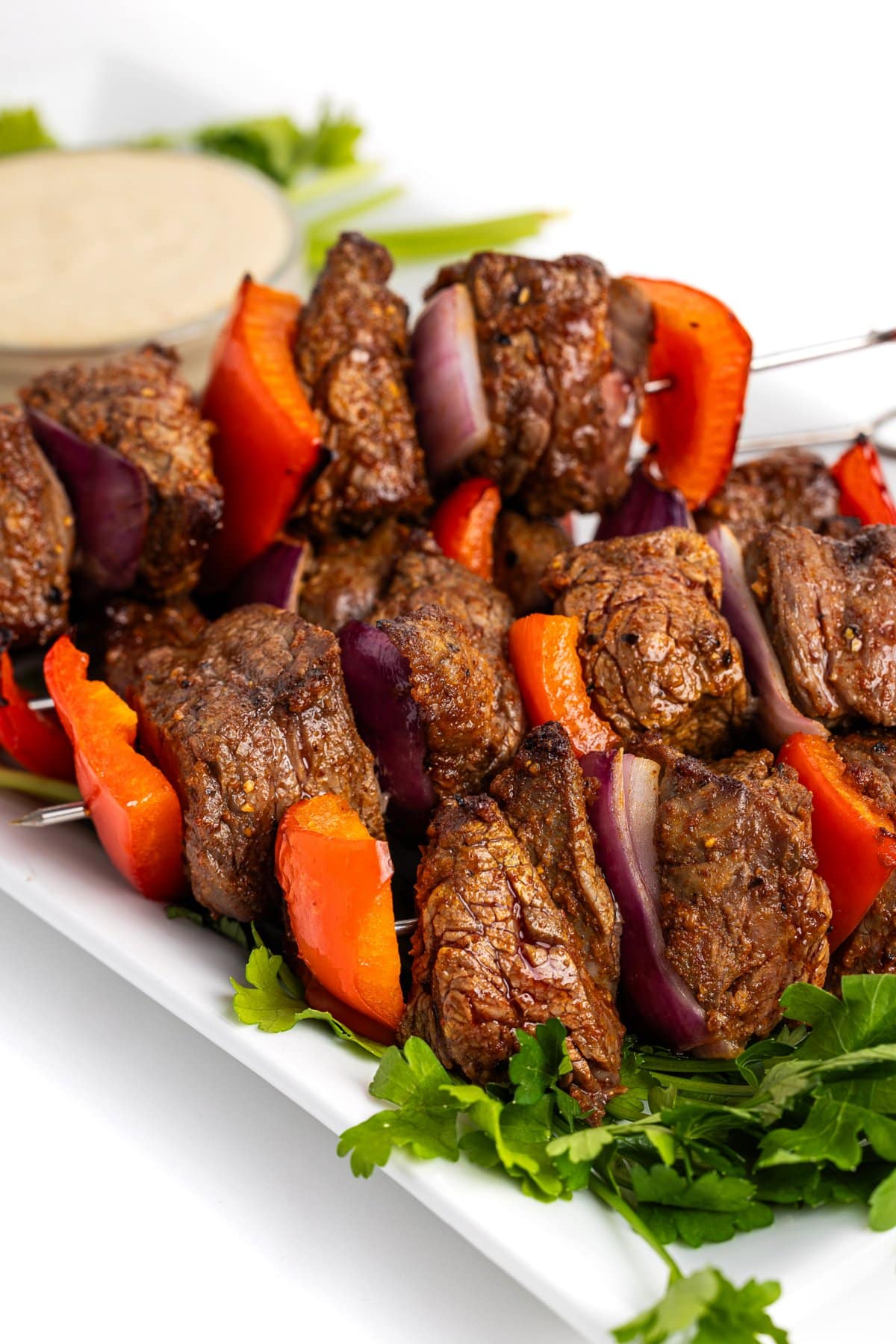 Broiled steak skewers with tahini sauce on a platter.