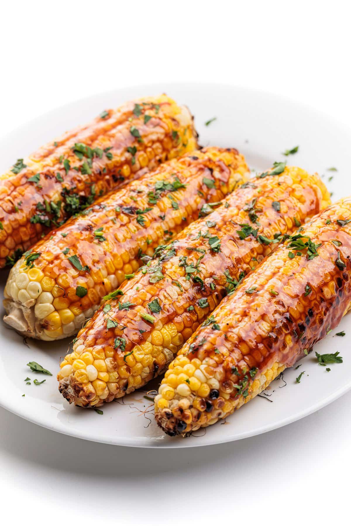 Close up shot of grilled corn with bbq sauce garnished with fresh parsley.