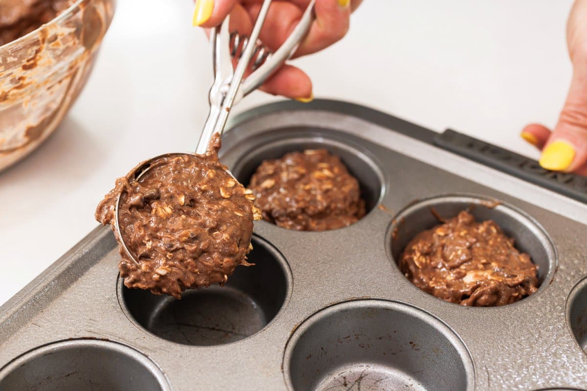 Scooping chocolate muffin batter into muffin tin.
