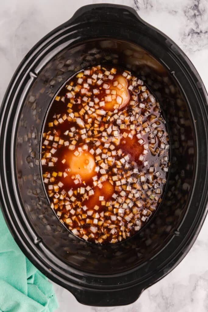 Raw chicken and diced onions in sauce in a slow cooker.