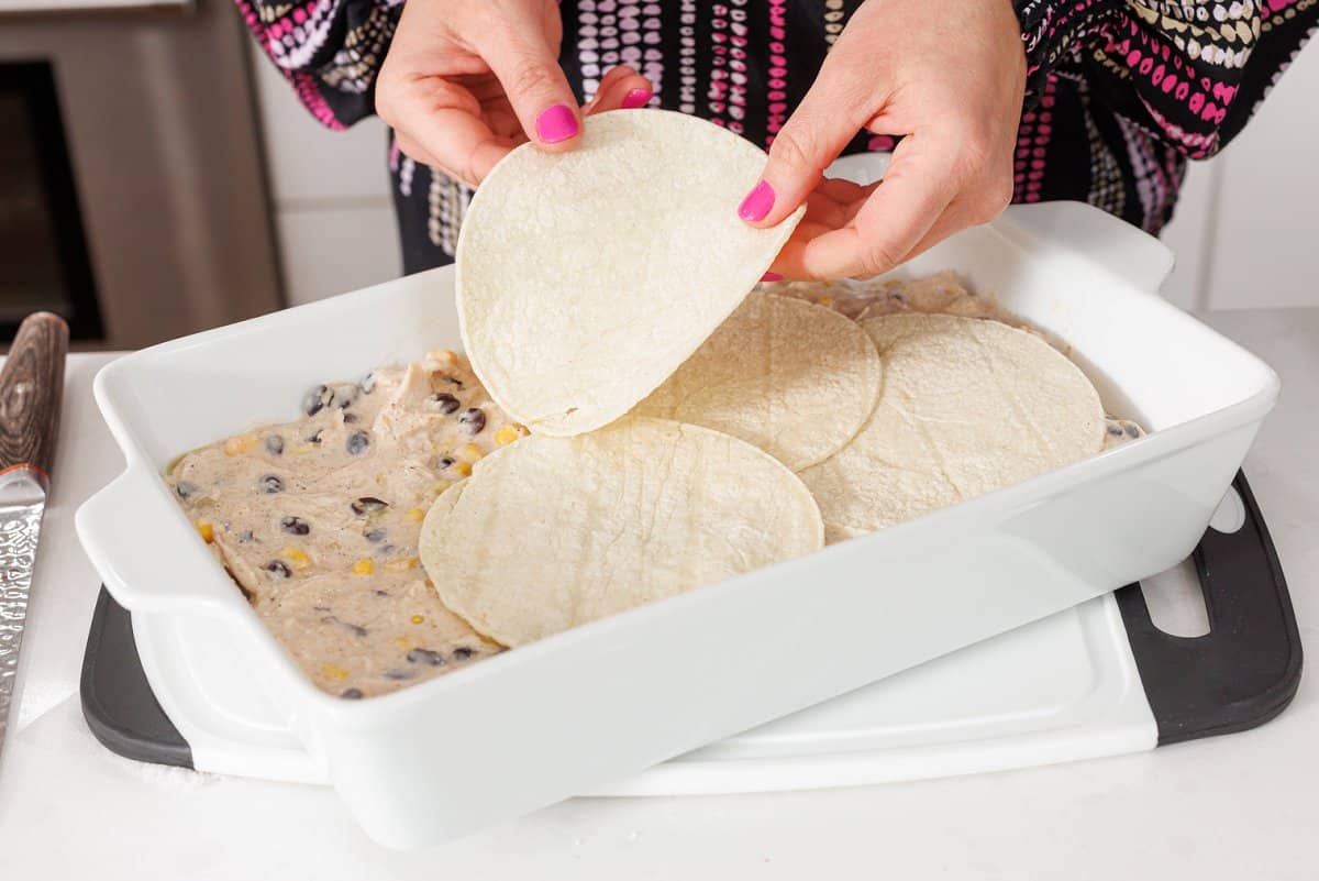 Laying tortillas on top of lasagna filling in casserole dish.