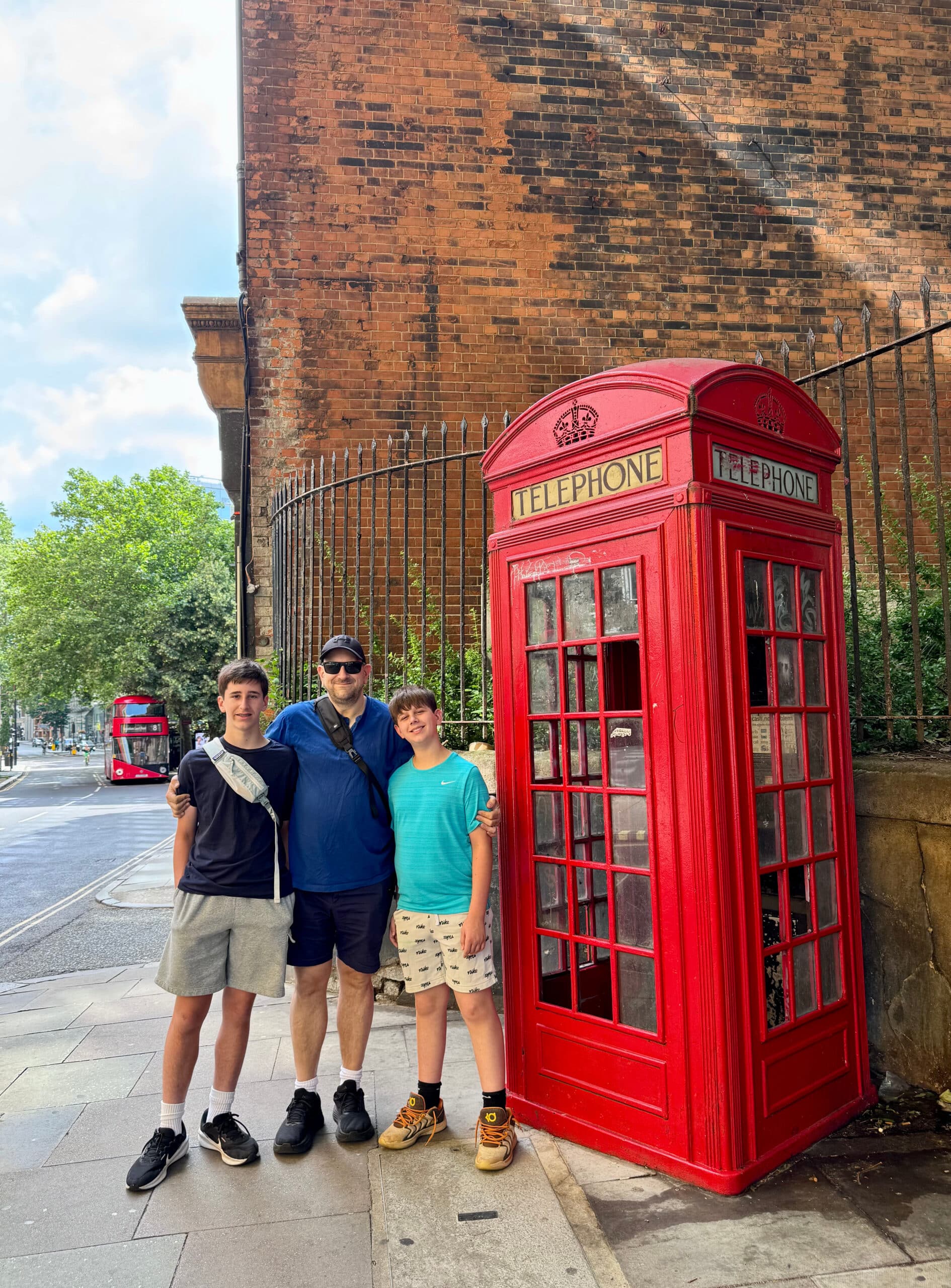 The boys standing in front of a red phone booth in London.