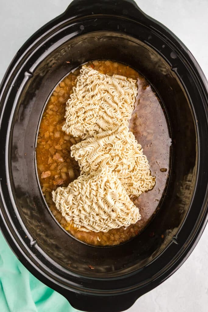 Dry ramen noodles added to a slow cooker with broth and onion mixture.