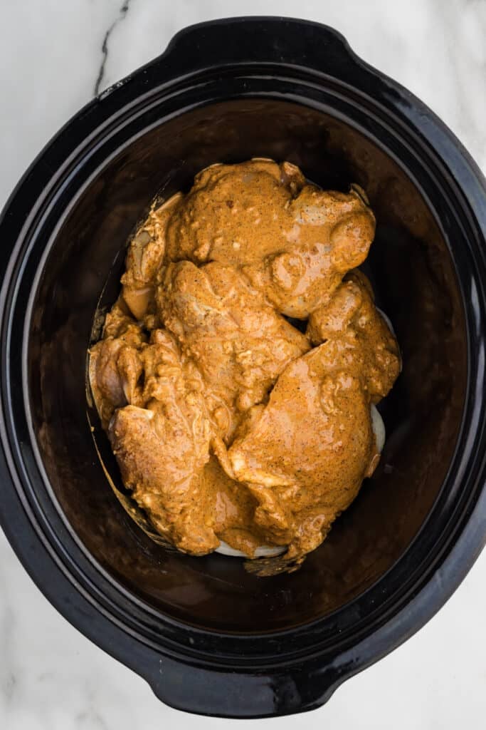 Raw marinated chicken thighs in a slow cooker ready to be cooked.