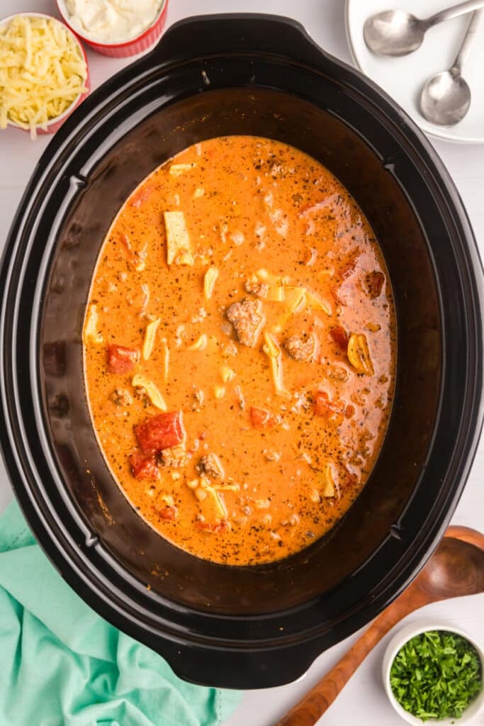 Slow cooker filled with lasagna soup, surrounded by toppings.