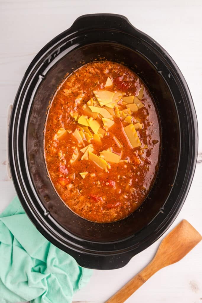 Uncooked pasta added to lasagna soup in a slow cooker.