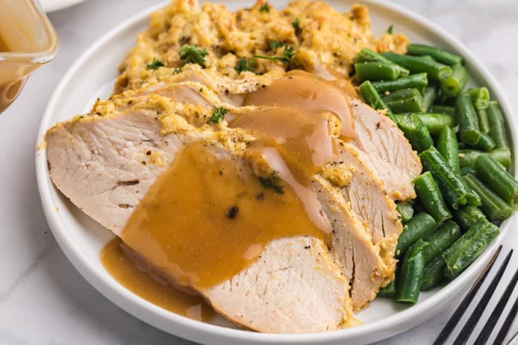 Sliced turkey with stuffing, green beans, and gravy on a white plate.